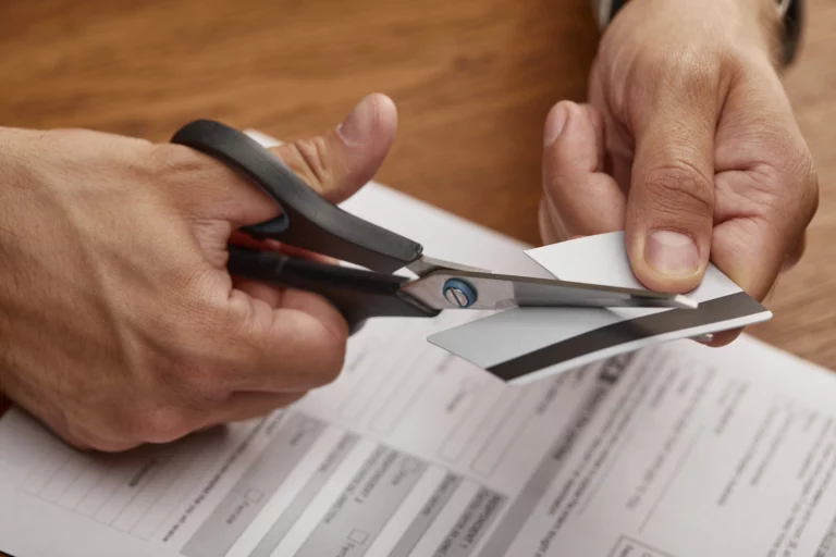A person cutting a credit card with scissors over a wooden table, symbolizing financial decision-making and debt relief.