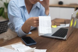 Person in a blue shirt carefully reviewing a receipt at a wooden table with papers and a smartphone, illustrating financial planning, budgeting, and Chapter 13 repayment plan management in Denver bankruptcy cases.