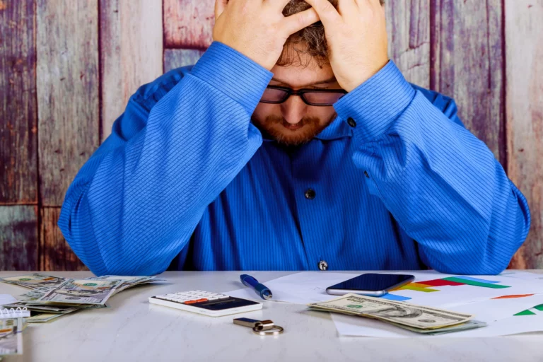 Man overwhelmed by debt reviews bills, cash, and financial documents while comparing Chapter 7 and Chapter 13 bankruptcy options in Denver